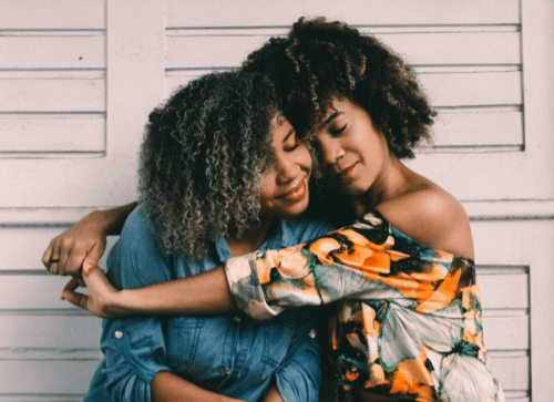 one girl gives another girl a hug, both are smiling