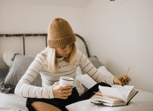 settle in at home - woman sitting on bed with coffee and notebook