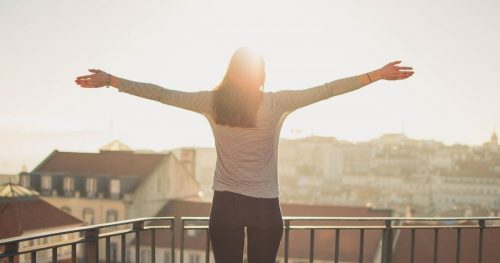 woman stretching out her arms to the sun on a balcony