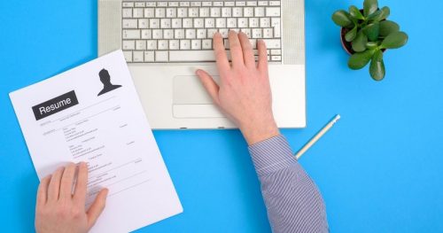 man holding resume typing on laptop