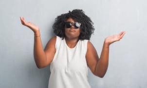 Black woman with sunglasses in a white sleeveless top showing a confused expression with her hands raised to her sides