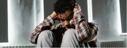 Young black man with hearing loss feeling overwhelmed holding his ears whilst sitting on the floor