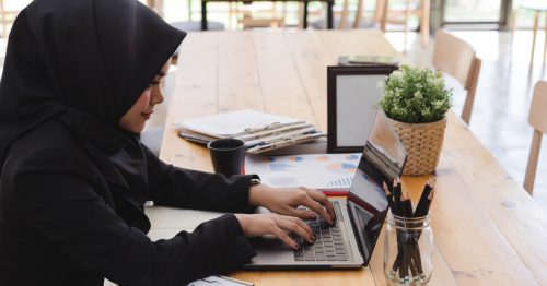 a muslim with deafness woman working at her desk with a laptop and assorted papers