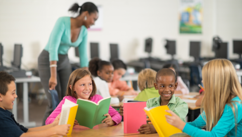 Classroom of 8 year old deaf children reading various coloured books with a black teacher in the background