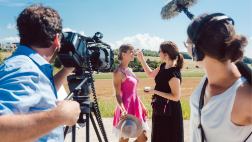 a deaf white woman having some makeup touched up with a camera and a boom mic in the foreground