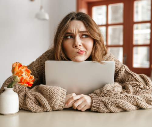 White woman in a big jumper slumped over her laptop looking confused when remote working
