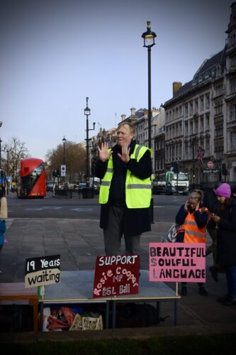 Role model David, standing in Central London in a rally, wearing a high-vis jacket signing to the crowd