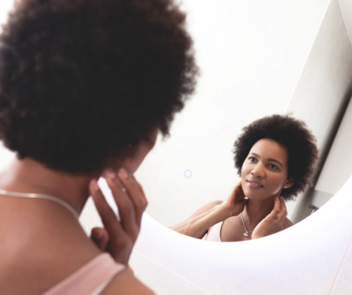 A deaf woman of colour looking at herself in the mirror