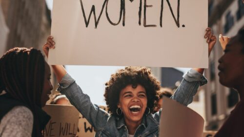 A black woman holding a sign saying WOMEN amongst a crowd