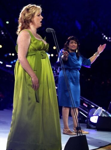 A woman in a green dress singing stands next to a woman in a blue dress signing
