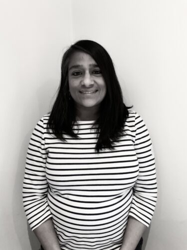 Black and white, a woman stands smiling, wearing a striped jumper